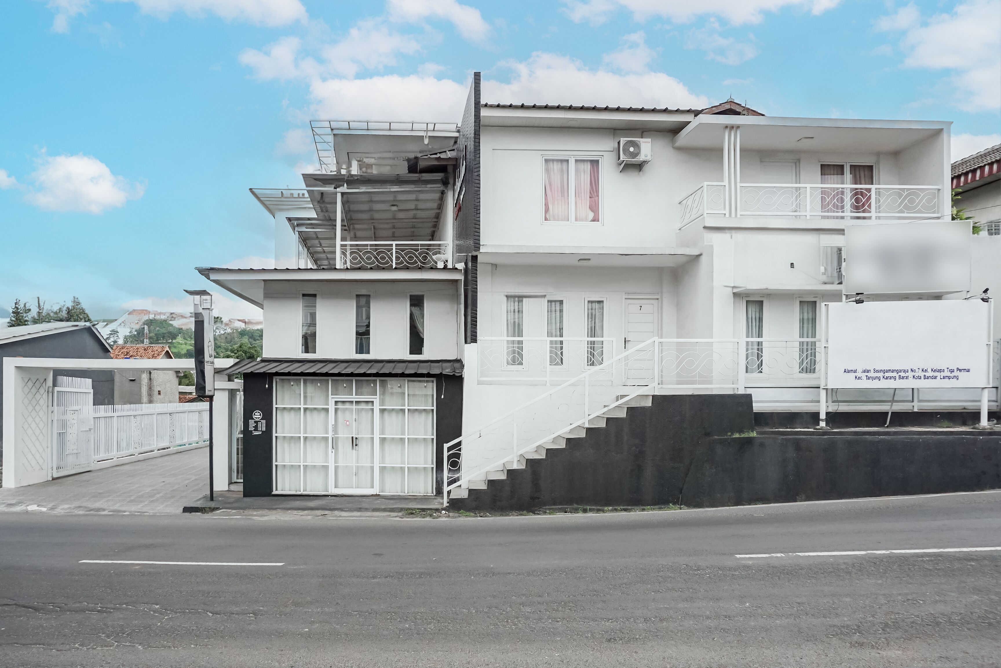 A two-story building with a white facade, a balcony on the upper floor, and a staircase leading to the entrance.