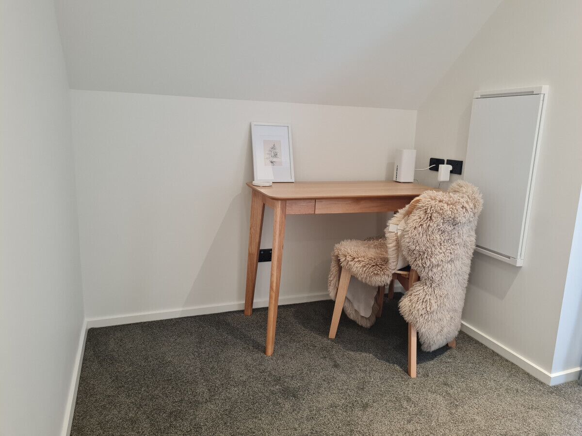 A small, neatly arranged room with a wooden desk, a chair, a framed picture, and a whiteboard.