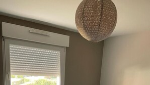 A bedroom with a bed, a window with blinds, a hanging light fixture, and a radiator. - SEVRIER, Bel appartement de 73M2 de 2 chambres pour 4 personnes avec parking et terrasse avec vue sur les montagnes, situé à 500m de la piste cyclable et du lac... (Sévrier)