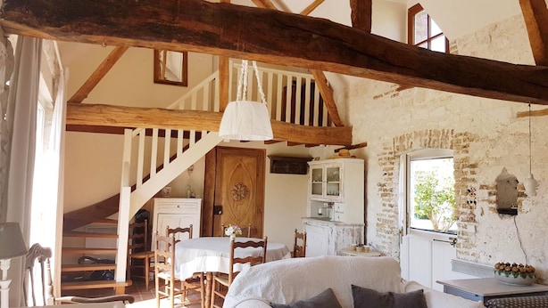 Ein rustikaler Raum mit freiliegenden Holzbalken, einer Treppe, einem Essbereich und einer gemütlichen Sitzecke mit einem Bett.