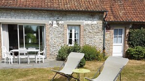 Ein Haus aus Stein mit Ziegeldach, einer Terrasse mit Stühlen und einem kleinen Tisch.