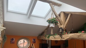 A room with a high ceiling, skylights, a wooden beam structure, a hanging plant, and a round window. - "carpe Diem" en Albret, Magnifique Longère Avec Piscine et Grand Terrain Clos (Espiens)