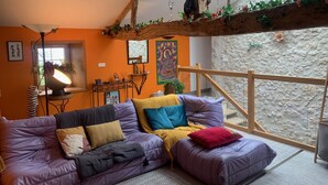 A cozy living room with a purple sofa, a wooden ceiling, and a stone wall. - "carpe Diem" en Albret, Magnifique Longère Avec Piscine et Grand Terrain Clos (Espiens)