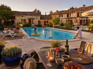 Un espace piscine agrémenté de bâtiments en pierre, de chaises longues et d’une table où sont servis des boissons et des collations.