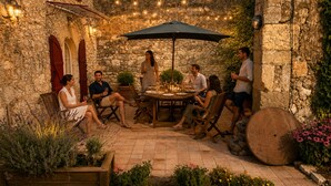 A stone-walled courtyard with a round table, outdoor seating, and string lights. - "carpe Diem" en Albret, Magnifique Longère Avec Piscine et Grand Terrain Clos (Espiens)