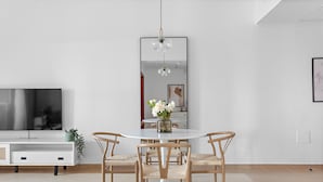 Ein moderner Essbereich mit einem runden Tisch, vier Holzstühlen, einer zentralen Vase mit Blumen, einer Hängeleuchte und einem großen Spiegel an der Wand.