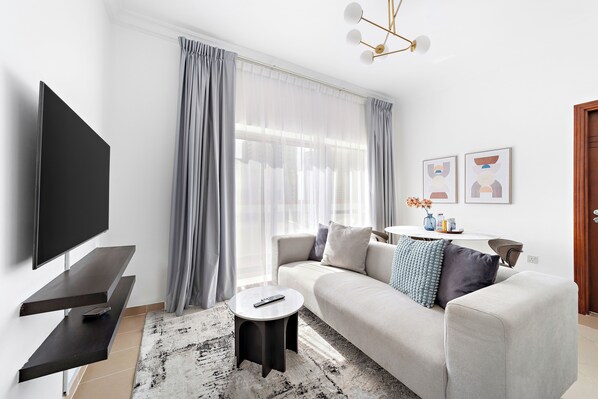 A modern living room with a flat-screen TV, a sofa, a coffee table, and a large window with curtains.