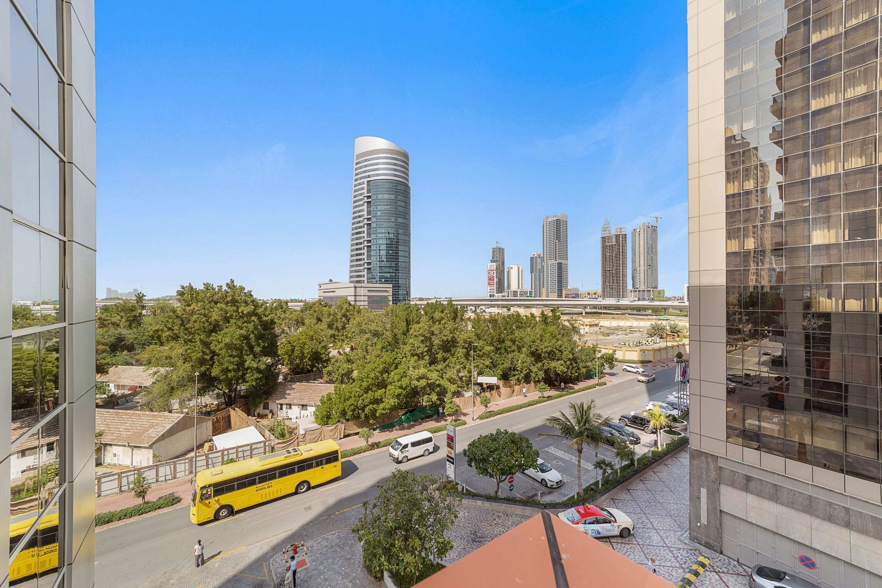 Une vue urbaine avec des bâtiments modernes, un autobus jaune et un ciel bleu dégagé.