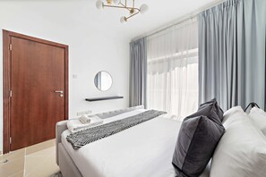 A modern hotel room with a large bed, a wooden door, a mirror, and a window with curtains.