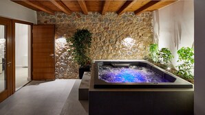 A spa area with a stone wall, a wooden ceiling, and a hot tub.