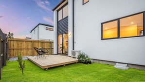 A modern house with a wooden deck, a small garden, and a large window.
