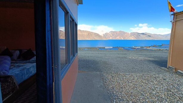 Habitació amb un llit i una finestra que dona a un massís d'aigua i muntanyes.