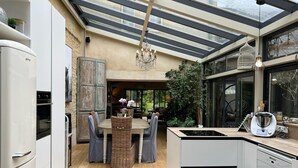A modern kitchen with a glass ceiling, a dining area with wicker chairs, and a built-in dishwasher. - Hidden gem in Bayeux : 3 bedrooms, backyard and spa -  king and queen size beds (Bayeux)