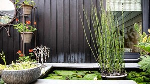 A garden with a pond, potted plants, and a mirror on a wooden wall. - Hidden gem in Bayeux : 3 bedrooms, backyard and spa -  king and queen size beds (Bayeux)