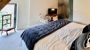 A bedroom with a sloped ceiling, a bed with a dark quilt, a television on a wooden stand, and a chair. - Hidden gem in Bayeux : 3 bedrooms, backyard and spa -  king and queen size beds (Bayeux)