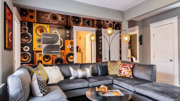 Ein modernes Wohnzimmer mit einem Ecksofa, einem Couchtisch und einer Wand, die mit Vintage-Lautsprechern dekoriert ist.