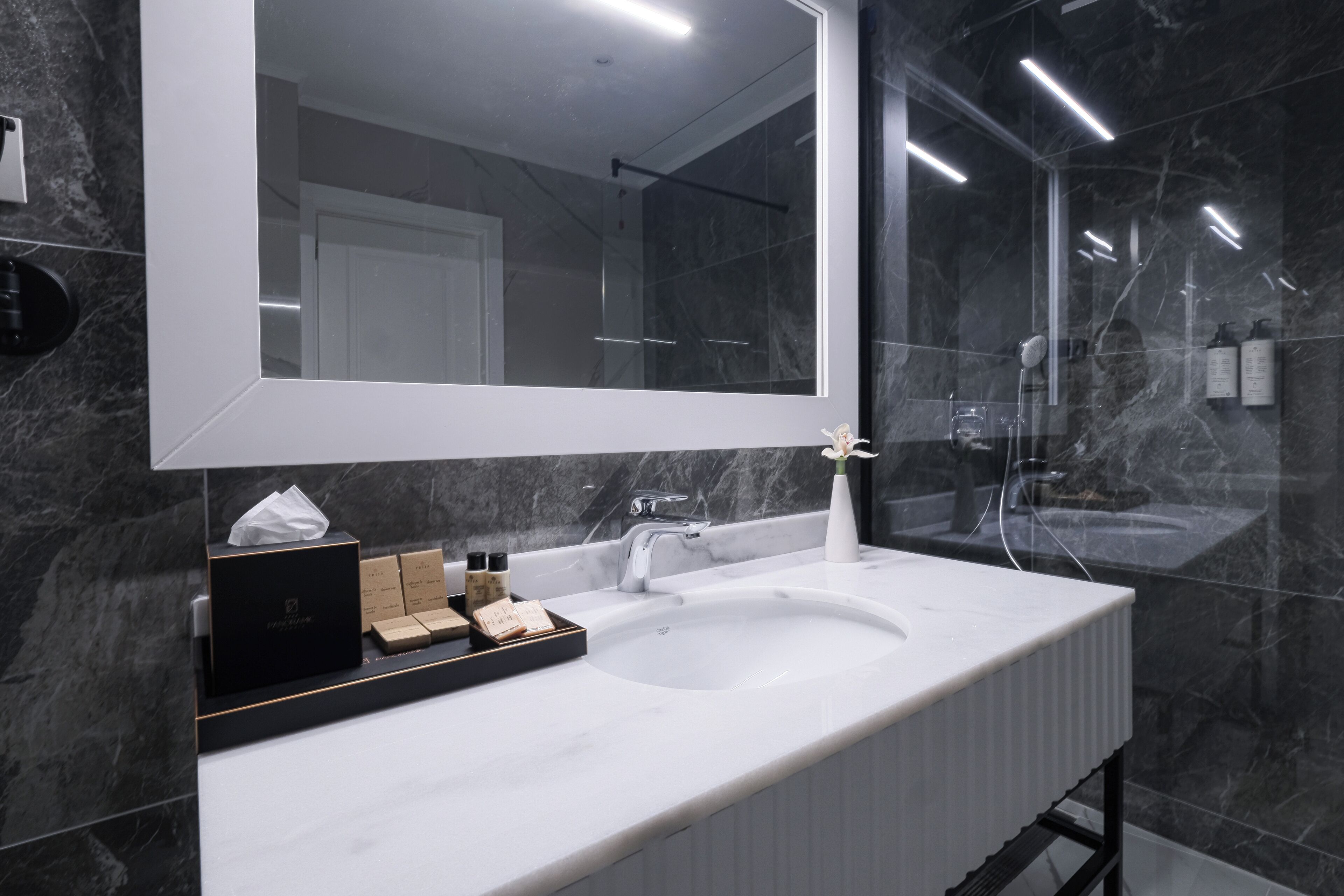 Une salle de bain moderne avec un grand miroir, un lavabo blanc et des murs en marbre.