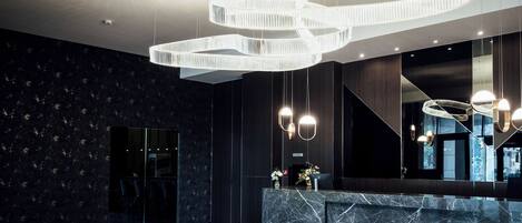 A modern lobby with a marble reception desk, a glass partition, and a unique circular light fixture.