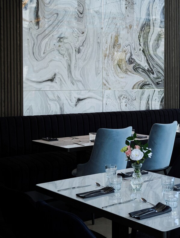 A restaurant interior with marble walls, dark upholstered booths, and a table set for two with a vase of flowers.