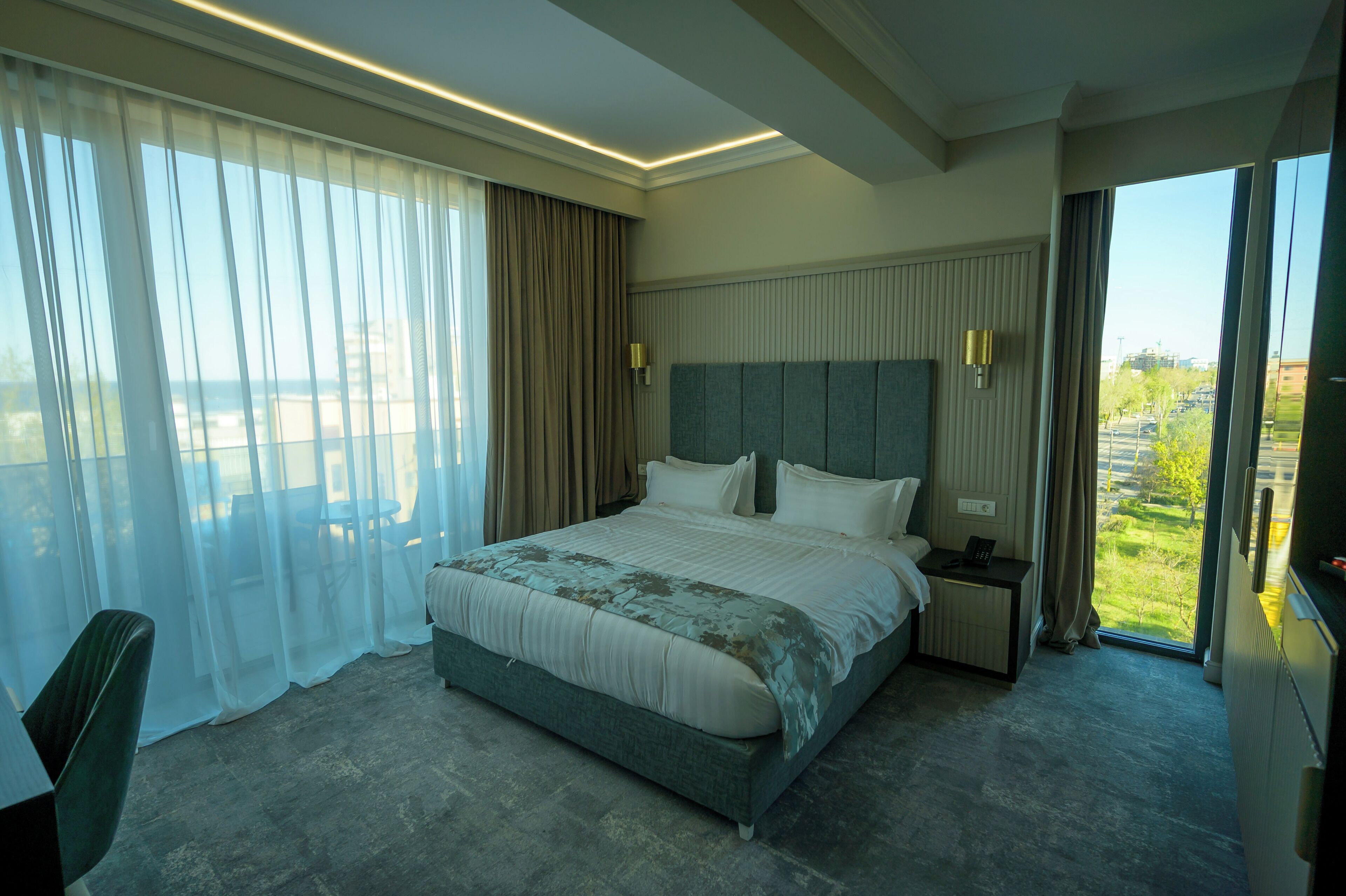 A modern hotel room with a large bed, a bedside table, a chair, and a view of the outdoors.