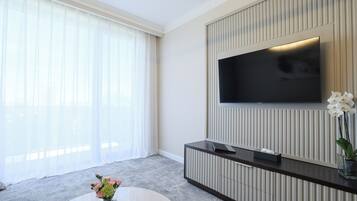 A modern living room with a large flat-screen TV mounted on a wall, a dark wooden console table, and a vase with flowers on a round coffee table.