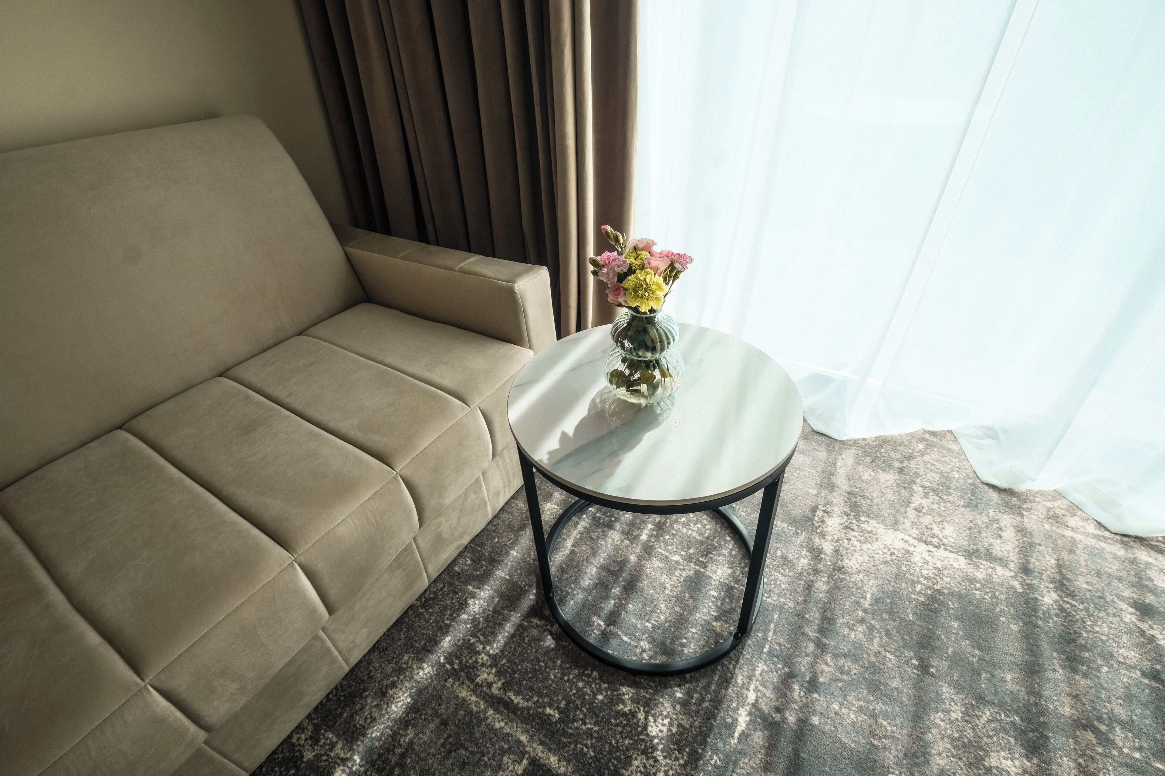 A beige sofa, a round glass table with a black base, and a vase with flowers.