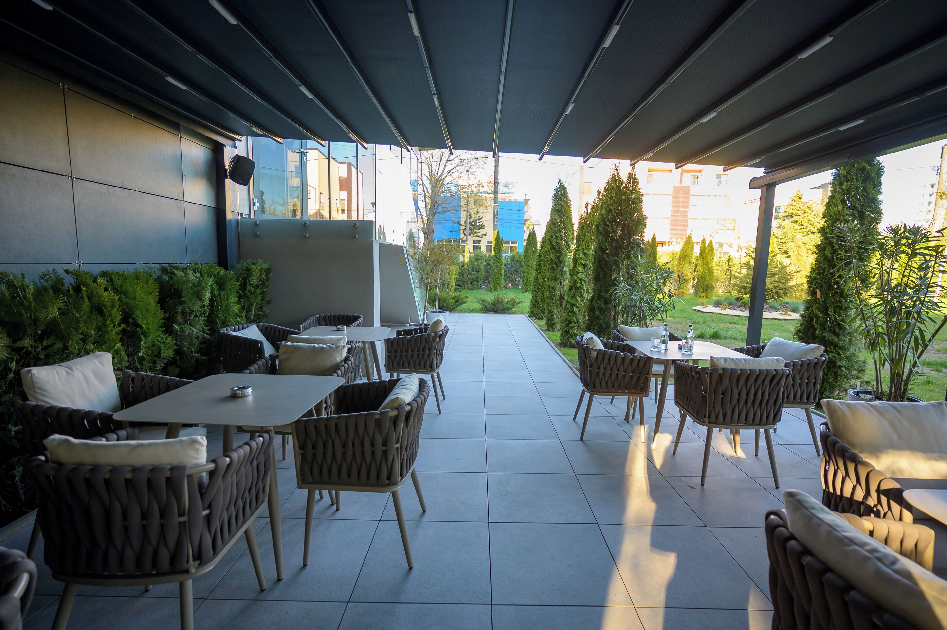 An outdoor patio with wicker furniture, a covered area, and a view of buildings and greenery.