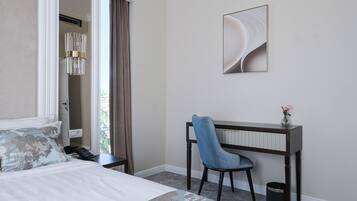 Habitación de hotel con cama, escritorio, silla, cesto de basura y un cuadro en la pared.