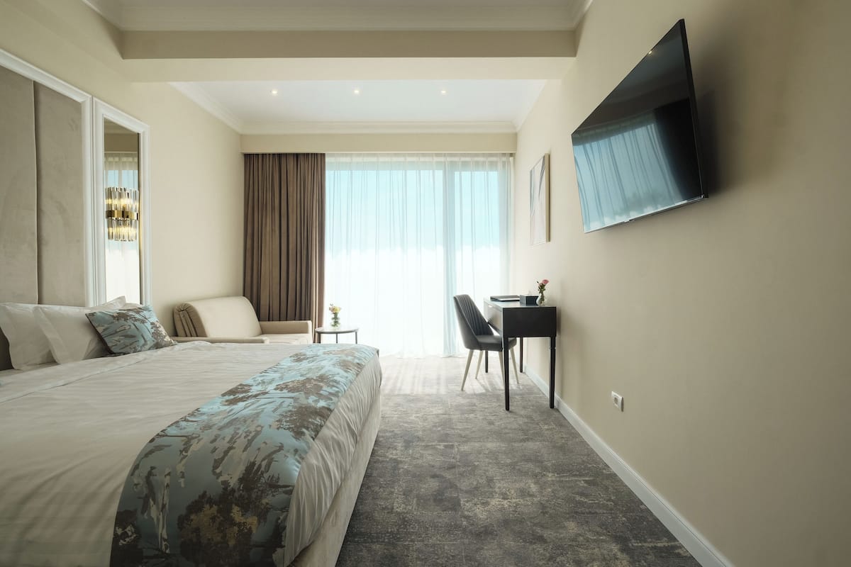 A hotel room with a large bed, a desk, a chair, and a TV mounted on the wall.