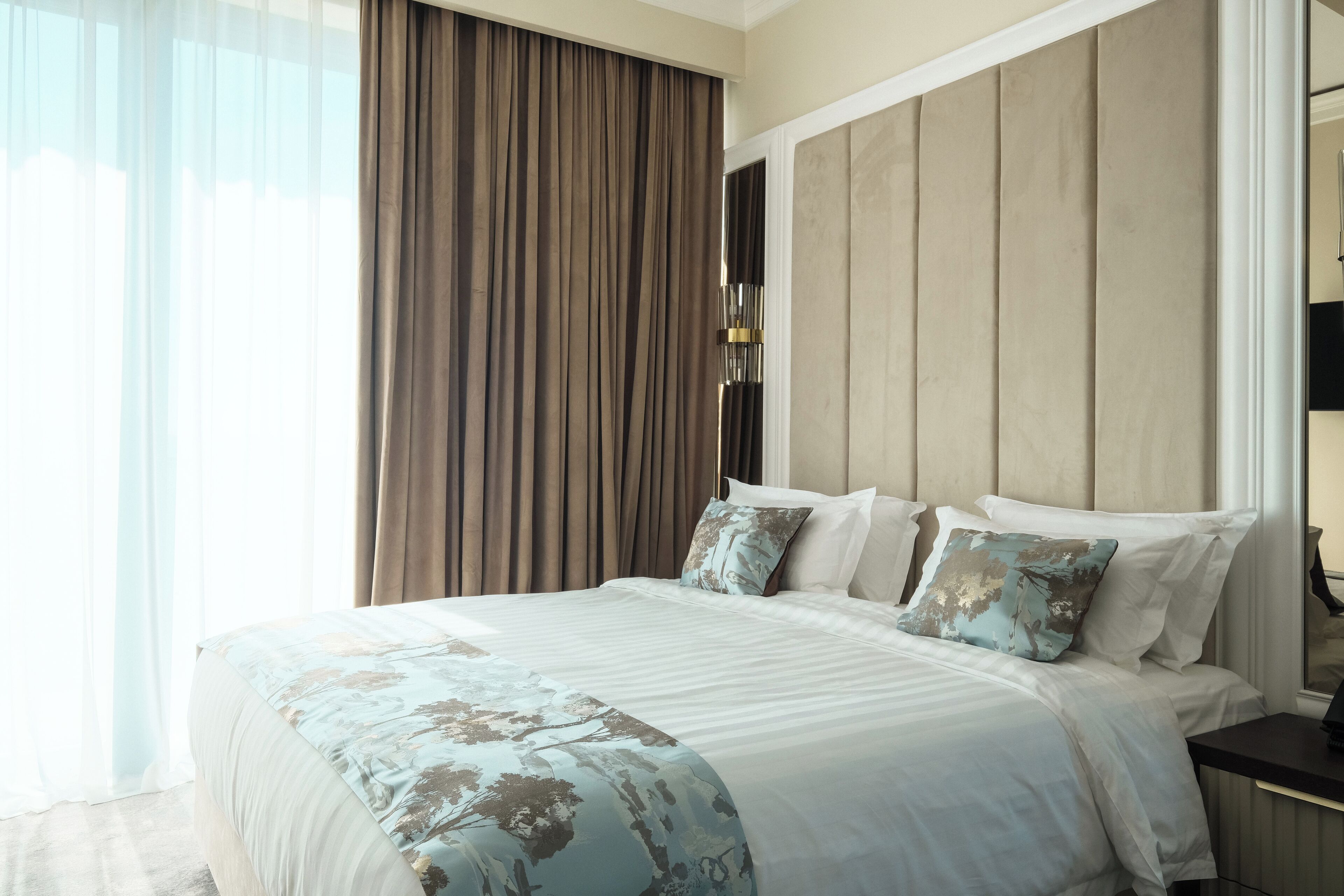 A modern hotel room with a large bed, a nightstand, and a window with curtains.