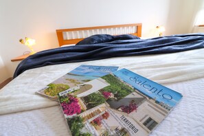 Una cama con un edredón azul oscuro, una colcha blanca y dos folletos de viaje sobre la misma.