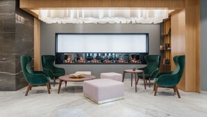 A modern living room with a large flat-screen TV, green upholstered chairs, a round coffee table, and a fireplace. - River Park Hotel (Cluj-Napoca)