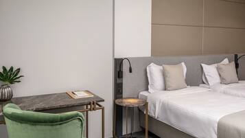 A hotel room with a bed, a green chair, a small table, and a potted plant.