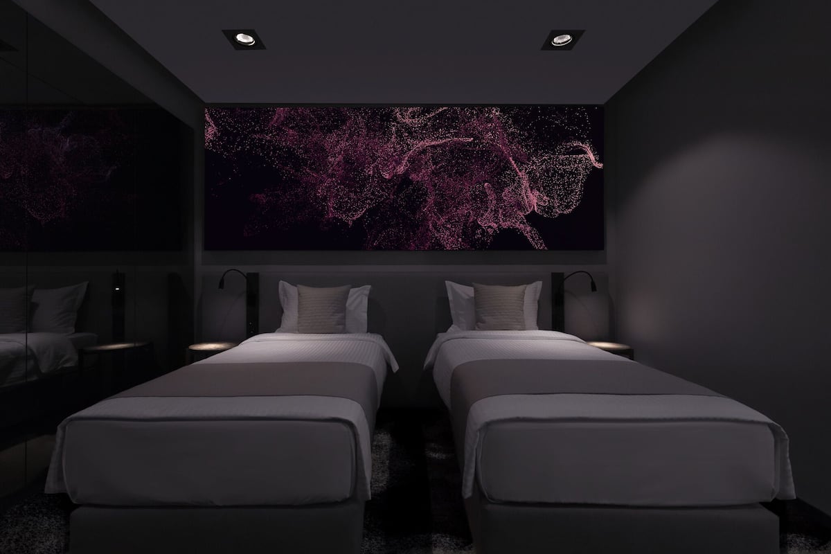 A modern hotel room with two beds, a large digital art display on the wall, and a dark color scheme.