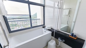 Un baño moderno con bañera, ducha, inodoro y ventana con vistas a la ciudad.