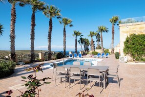 Relax by the pool with ocean views, surrounded by palm trees and a stone wall.