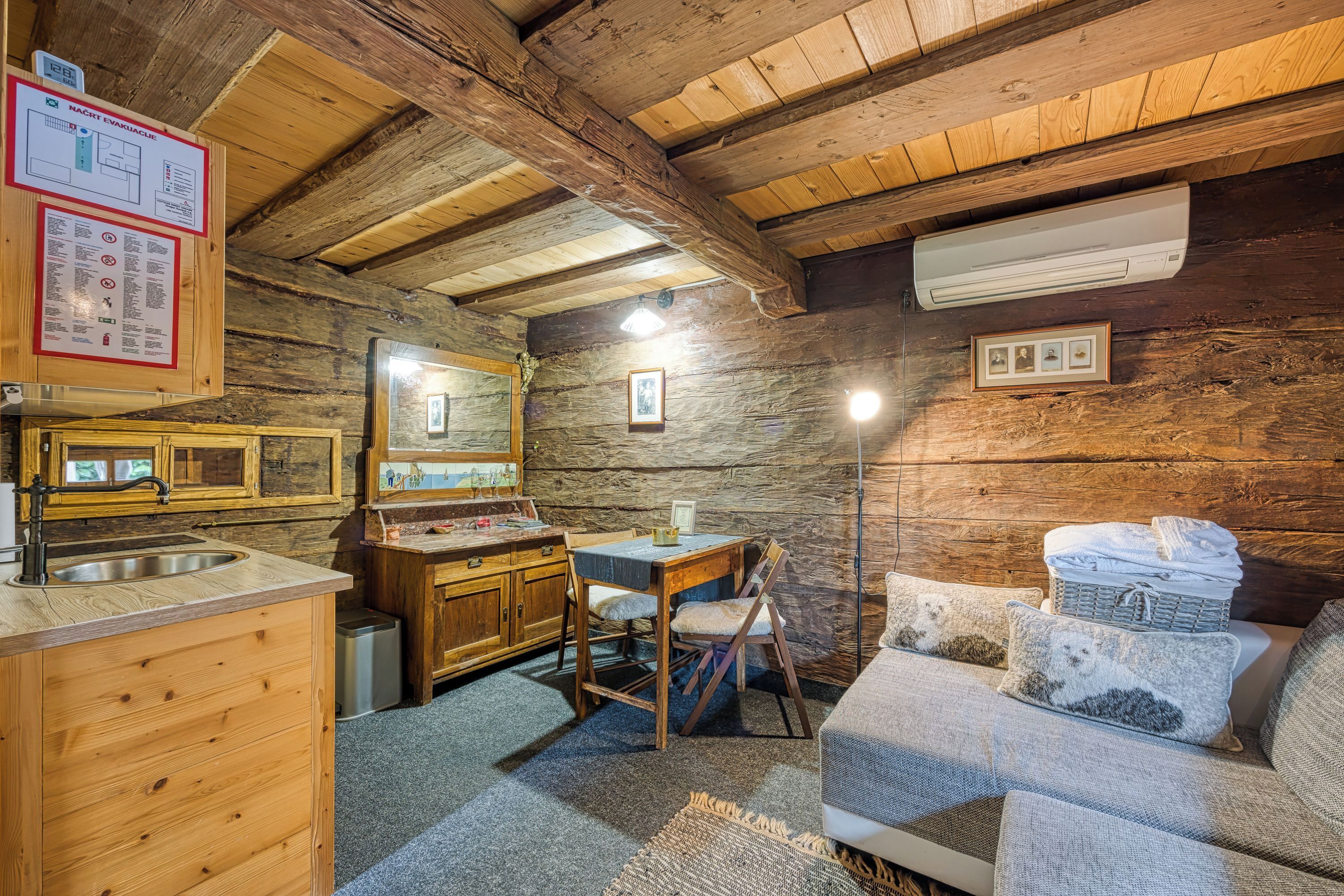 A rustic cabin interior with wooden walls, a wooden ceiling, a kitchenette, a sofa, and a framed picture on the wall.