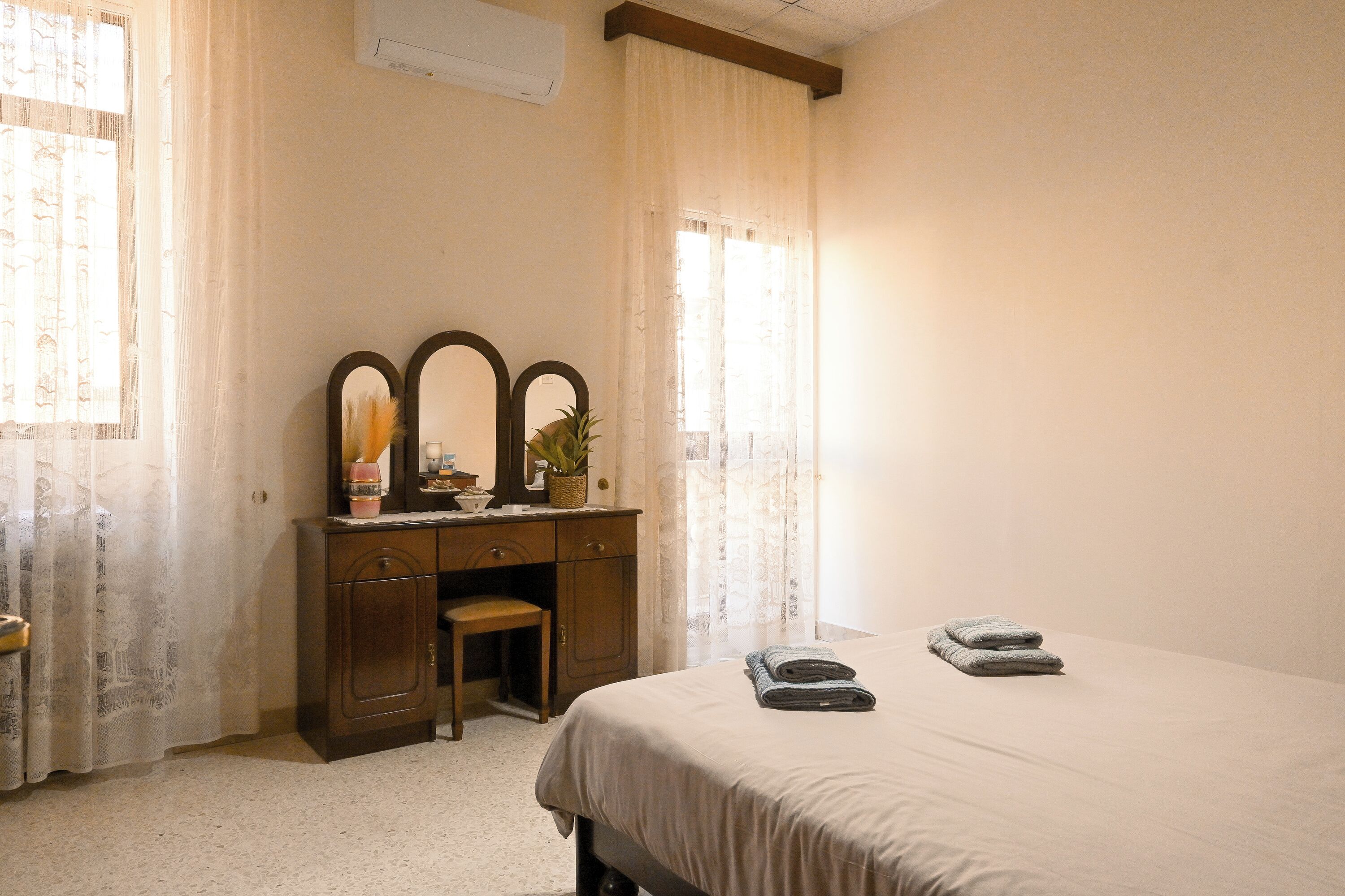 A bedroom with a bed, a wooden desk with a mirror, and a chair.