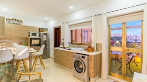 A modern kitchen with a built-in washing machine, dining area with chairs, and a view through a glass door. - Sunny Maltese Townhouse Madonnina Kalkara (Kalkara)