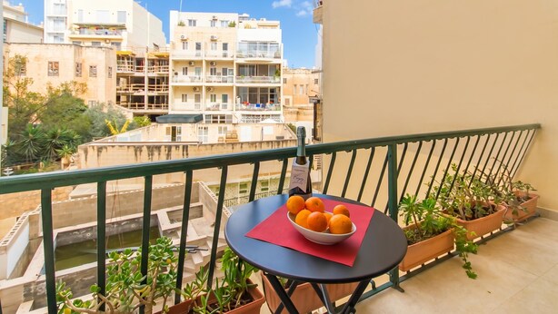 A balcony with a table, potted plants, and a bowl of oranges.