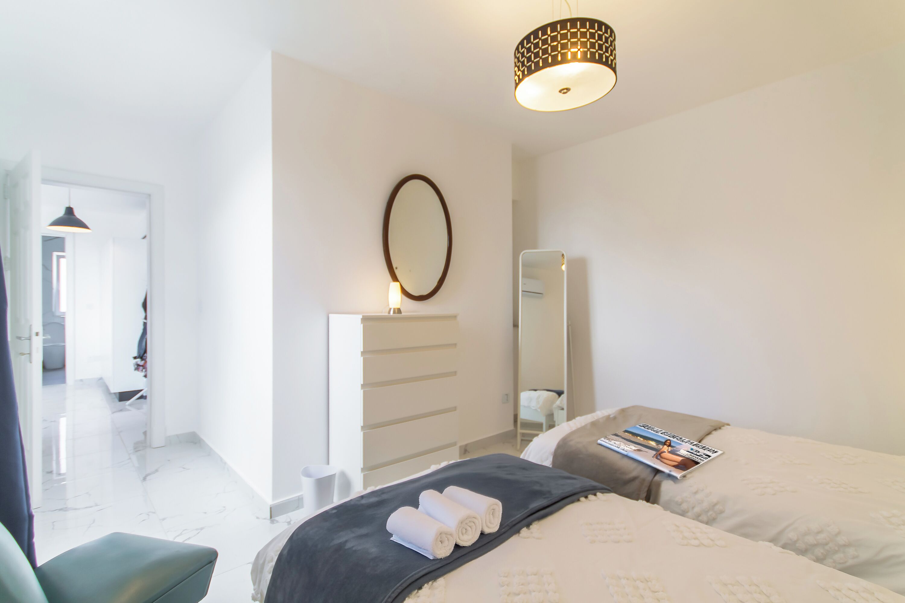 A hotel room with a bed, a dresser, a mirror, and a hanging light fixture.