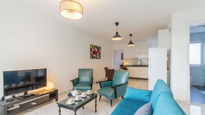Ein modernes Wohnzimmer mit Flachbildfernseher, einer Couch, zwei Sesseln, einem Couchtisch und Pendelleuchten.