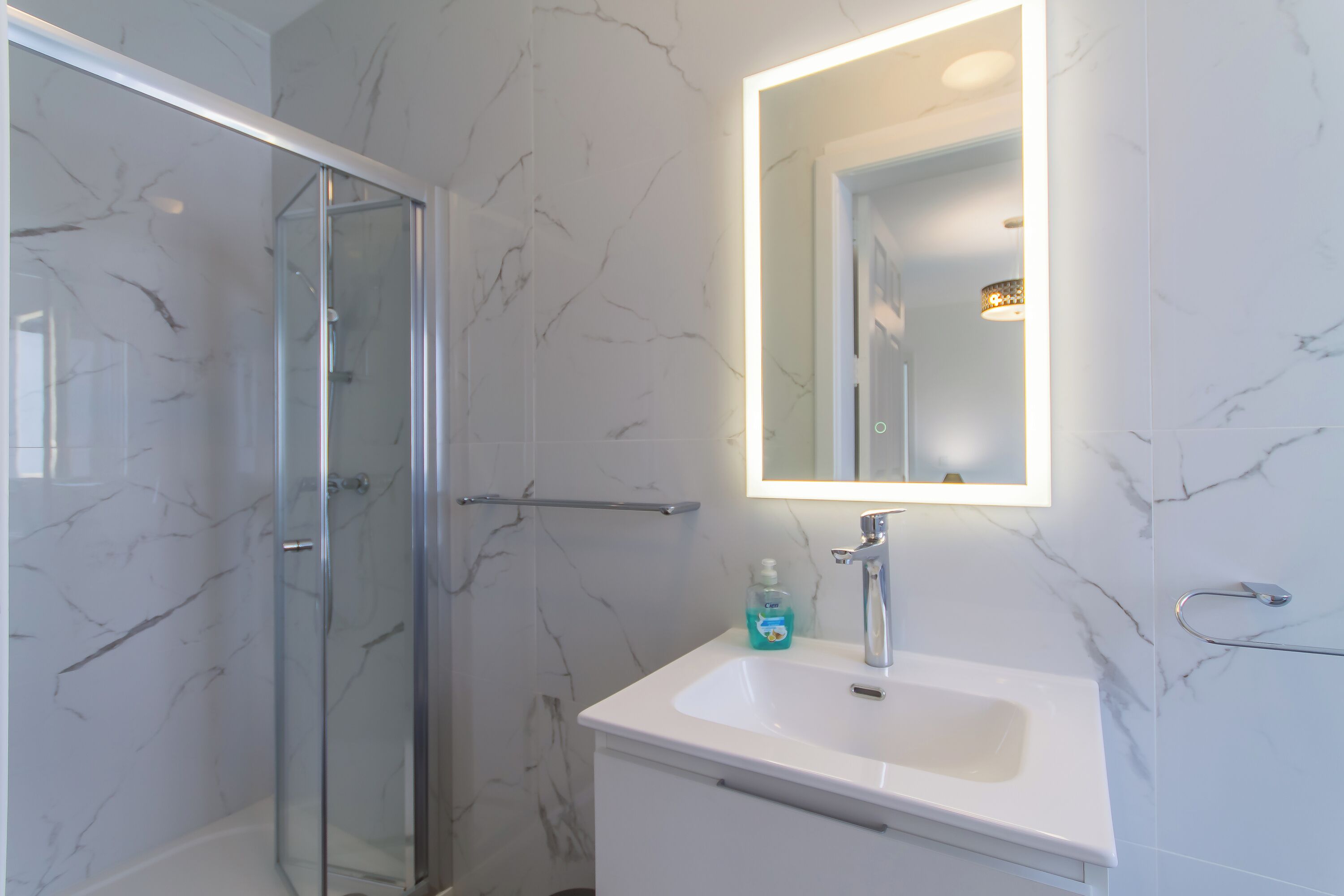 Un baño moderno con cabina de ducha de vidrio, un lavabo blanco y un espejo con luz integrada.