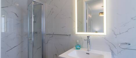 Un baño moderno con cabina de ducha de vidrio, un lavabo blanco y un espejo con luz integrada.