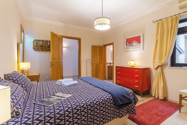 Un dormitorio con cama, mesita de noche, cómoda y ventana con cortinas.