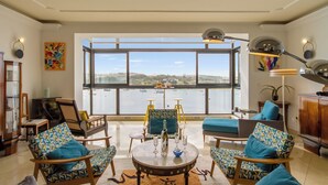 A spacious living room with a large window overlooking a body of water, furnished with patterned chairs and a round table. - A Magnificent Sunny Seafront Apart Sliema (Sliema)