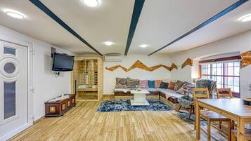 A modern living room with a wooden floor, a sofa set, a dining table, and a TV mounted on the wall.