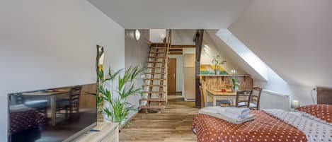 A bedroom with a wooden floor, a TV, a bed with polka dot bedding, a ladder, and a desk with a chair.