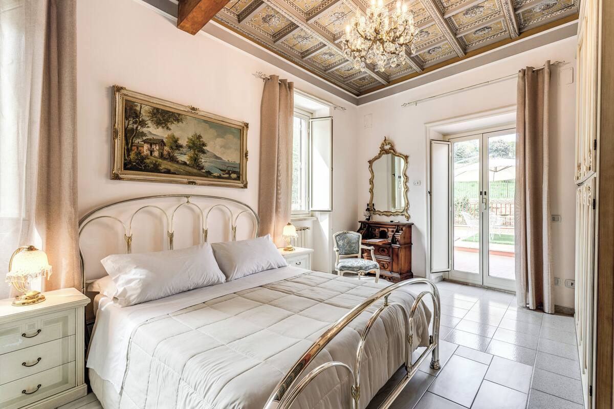 A bedroom with a bed, a nightstand, a chair, a dresser, a mirror, and a painting on the wall.