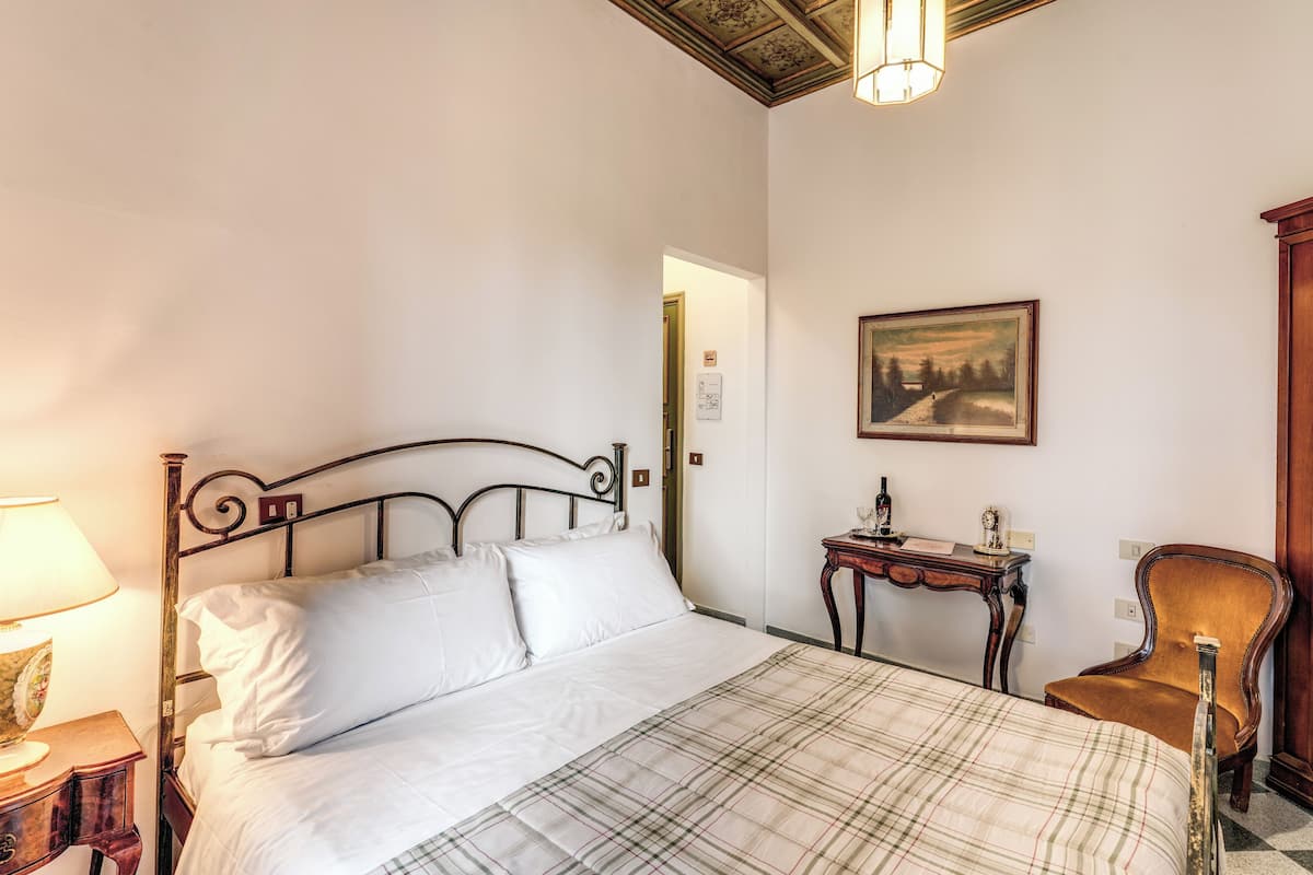 A bed with a plaid bedspread, a wooden nightstand with a lamp, a small table with a bottle, and a chair.